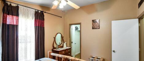 A bedroom with a bed, a wooden bench, a ceiling fan, a mirror, a door, and a white wall.