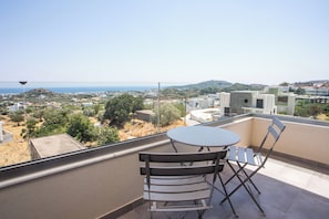 En balkon med et bord og stole, der kigger ud over en kystby med bygninger og grønne områder.