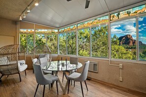 A room with a round glass table, grey chairs, a wicker chair, and large windows with a view of trees and mountains. - Spectacular Rental with Breathtaking Mountain Views in Arizona (Sedona)