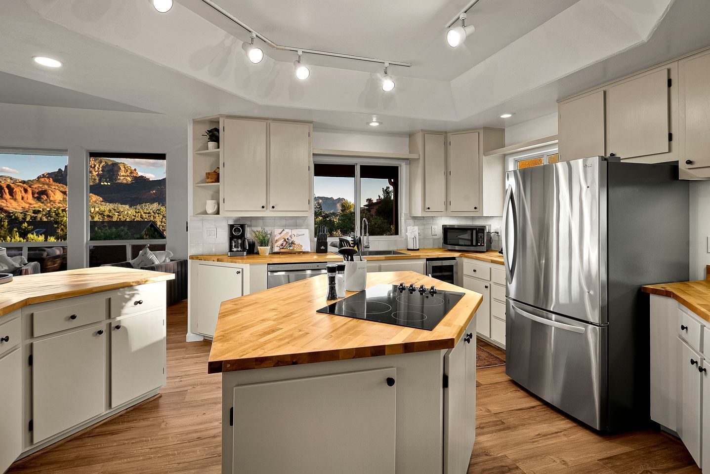 Una cocina moderna con armarios blancos, encimera de madera, electrodomésticos de acero inoxidable y vistas a un paisaje montañoso.