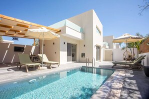 Un área de piscina moderna con sillones de descanso, sombrillas y agua cristalina.