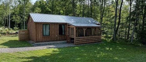 Una cabaña de madera con techo de metal, rodeada de césped y árboles.