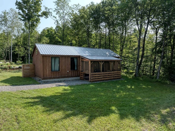 A wooden cabin with a metal roof, surrounded by a grassy area and trees.
