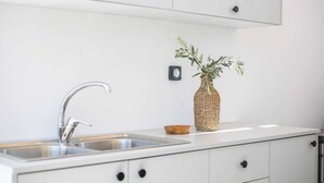 A kitchen with a stainless steel sink, white cabinets, a woven basket, and a small potted plant. - Aura Luxury Villas Anasa, Villa (Rhodes)