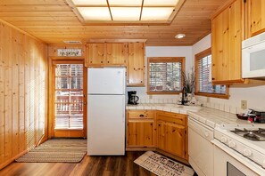 Eine Küchenzeile im Landhausstil mit Holzschränken, einem weißen Kühlschrank, einem Herd und einem Fenster mit Jalousien.