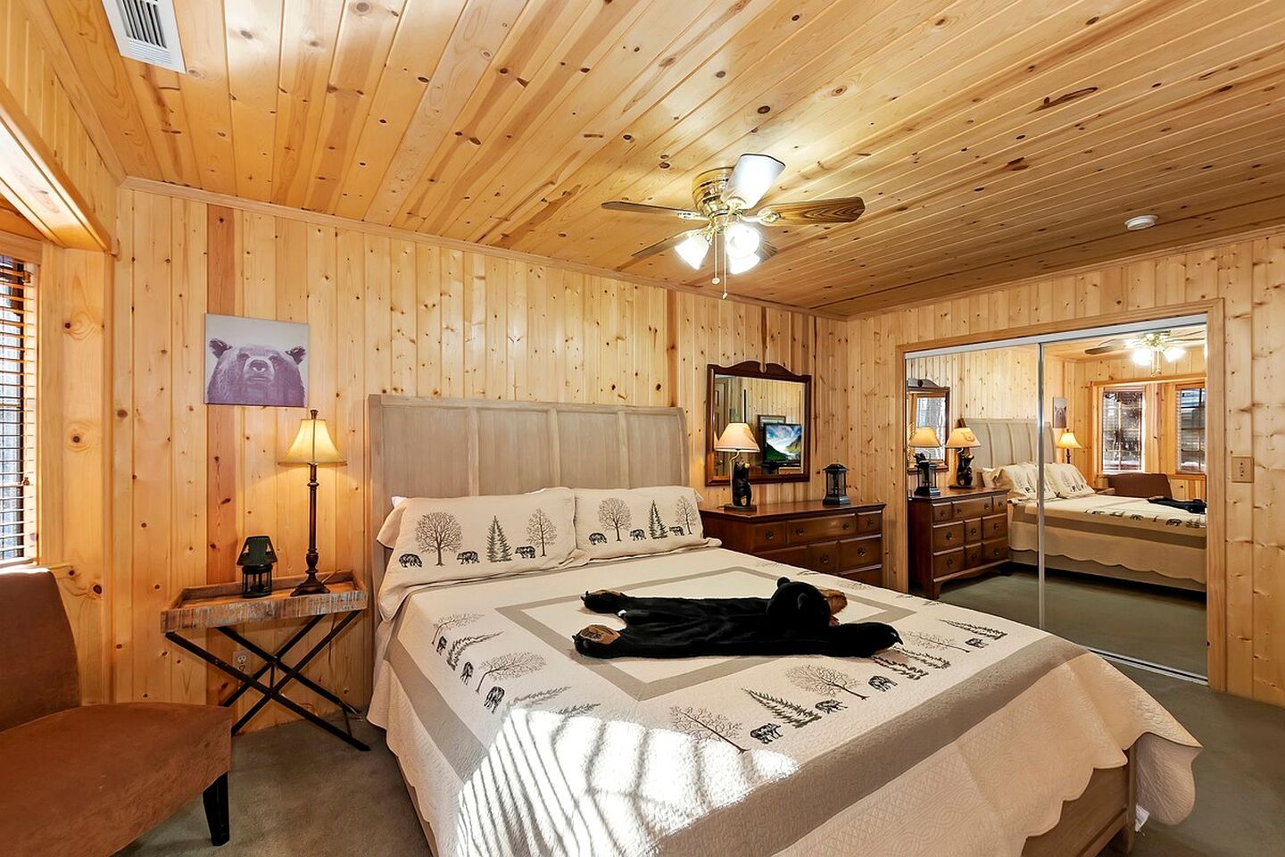 Un dormitorio con paneles de madera, una cama, mesitas de noche, un espejo y un ventilador de techo.