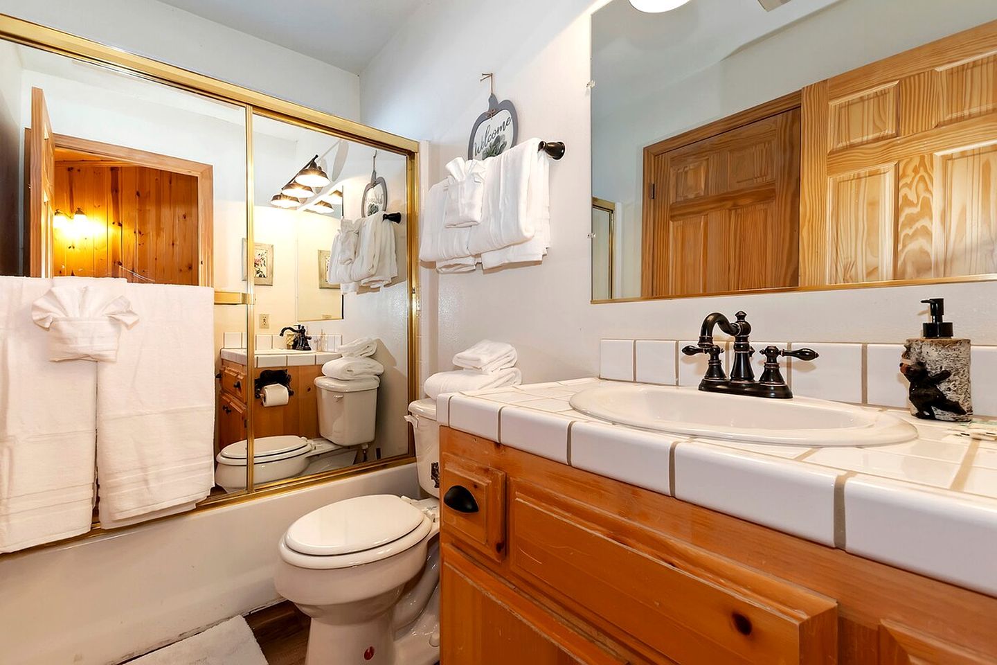 A bathroom with a wooden vanity, a large mirror, a sink with a black faucet, and a toilet.