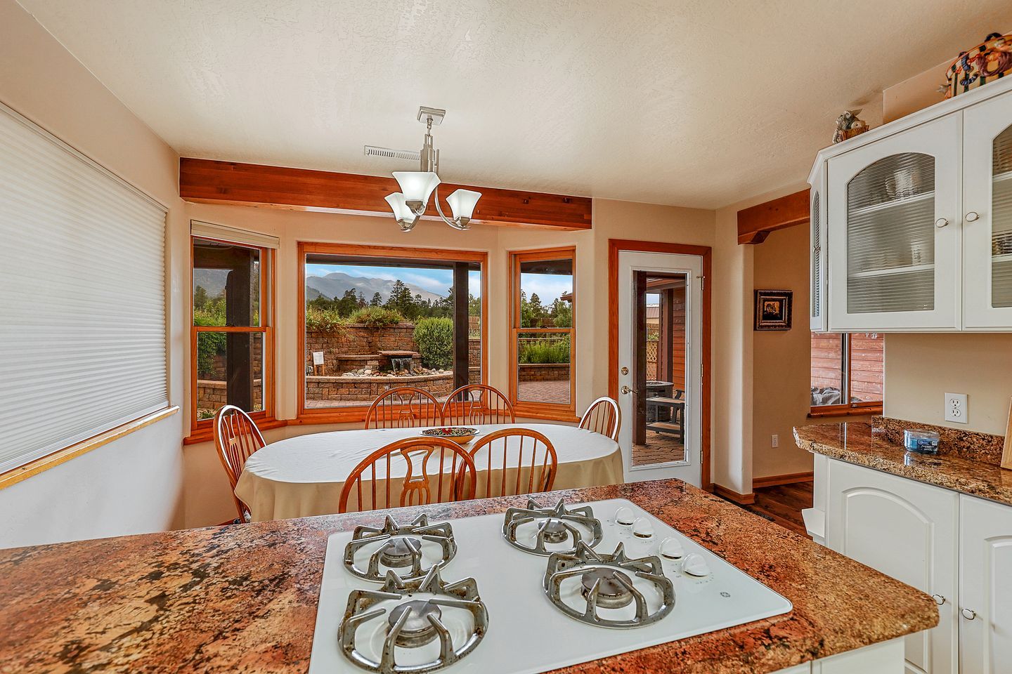 A kitchen with a gas stove, a dining table with chairs, and a view of a garden through large windows.