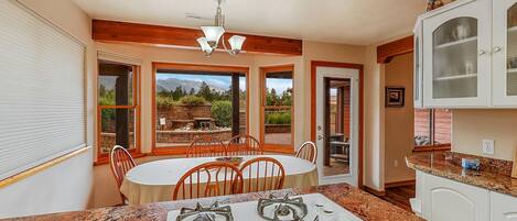 A kitchen with a gas stove, a dining table with chairs, and a view of a garden through large windows.