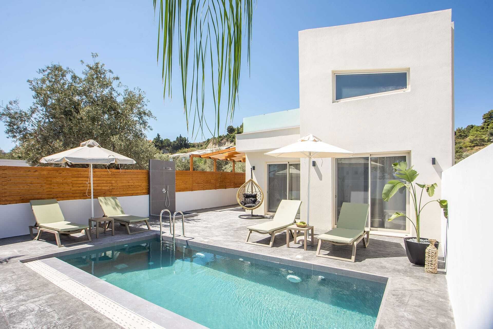Ein moderner Außenpoolbereich mit Liegestühlen und Sonnenschirmen, eine Holzlattenverkleidung und ein Gebäude mit großen Fenstern.