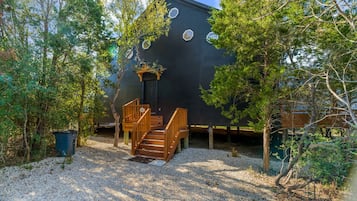 Ein Haus mit einer Holztreppe, die zu einer Tür führt, umgeben von Bäumen und Kies.