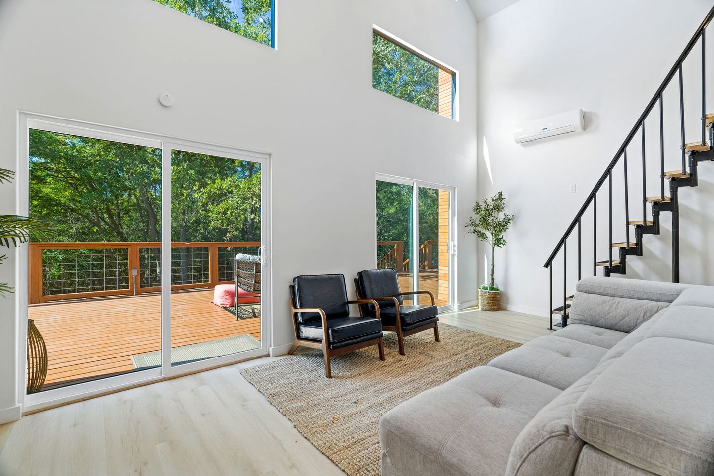 A spacious living area with a large sliding glass door leading to an outdoor deck, a staircase, and a modern interior design.