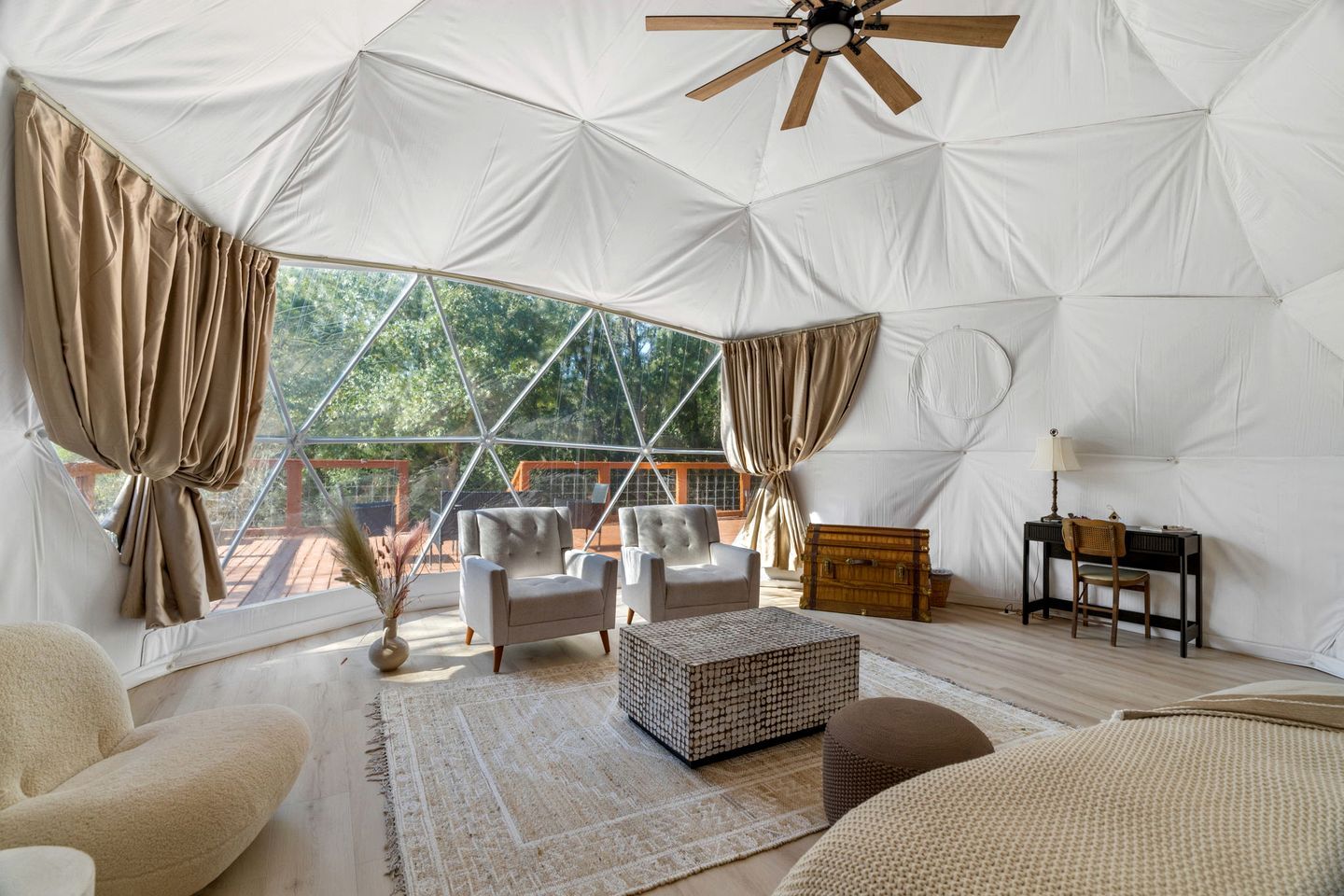 Habitación con tienda de campaña, ventilador de techo, dos sillones, una mesita, una lámpara y vistas a zonas verdes.