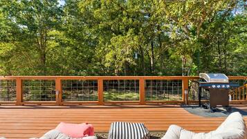 A deck with a grill, cushioned seating, and a wooden fence.