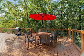 Eine Holzterrasse mit rundem Tisch, Stühlen, einem roten Sonnenschirm und einem Grill.
