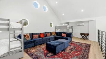 Een loft-achtige kamer met een blauwe modulaire bank, een kamerkleed met dessin en een stapelbed.