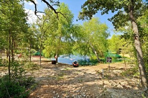 A campsite with a sign indicating no swimming in the pond, surrounded by trees and a clear sky.