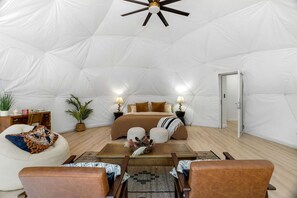 A spacious tent with a bed, two bedside tables, a chair, and a small table with a decorative item.