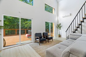 A spacious living area with a large sliding glass door leading to an outdoor deck, a staircase, and a modern interior design.
