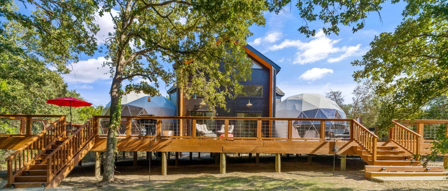 A modern wooden structure with a glass dome, wooden deck, and stairs.