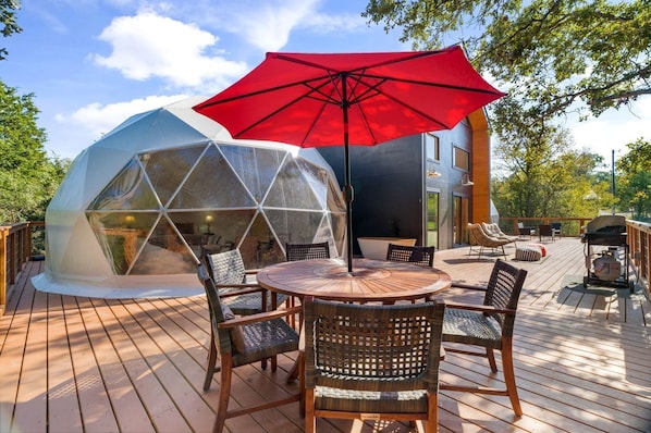 A geodesic dome structure with a wooden deck, outdoor seating, and a red umbrella.