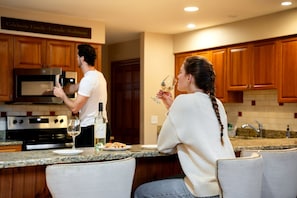 A modern kitchen with wooden cabinets, a stainless steel refrigerator, and a microwave. There is a bottle of wine and a glass on the counter. - Bretton Woods Vacation Rental near Mt Washington (Carroll)
