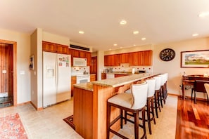 Una cocina moderna con armarios de madera, una isla central con taburetes altos, un microondas y un reloj en la pared.
