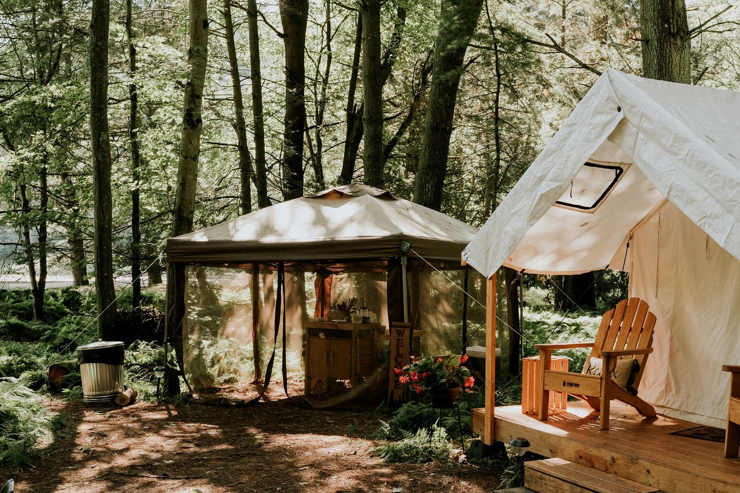 Campsite arbolado con una tienda de campaña, una terraza de madera y un letrero de bienvenida.