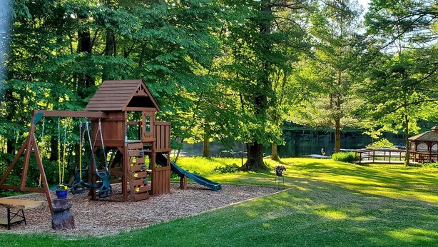 A wooden playground with swings and a slide, surrounded by trees and a picnic area.