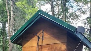 A wooden cabin with a small window, a door, and a metal device mounted on the wall.
