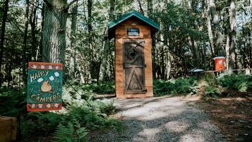 A rustic cabin labeled 'THE OTHOUSE' with a wooden door and a green roof, surrounded by a forest.