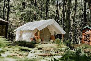 A forested area with a tent-like structure, a wooden chair, and a small building labeled 'The Outhouse.'