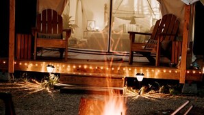 Una carpa con un hoyo para fuego al frente, sillas de madera y una guirnalda de luces a lo largo del borde delantero.