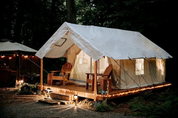 A tent with a porch, wooden chairs, and string lights.