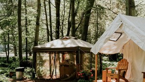 Campsite arbolado con una tienda de campaña, una terraza de madera y un letrero de bienvenida.