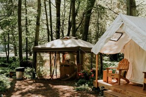Un terrain de camping boisé avec une tente, une terrasse en bois et un panneau d’accueil.