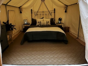 A tented room with a bed, bedside tables, a lamp, and a hanging light fixture.