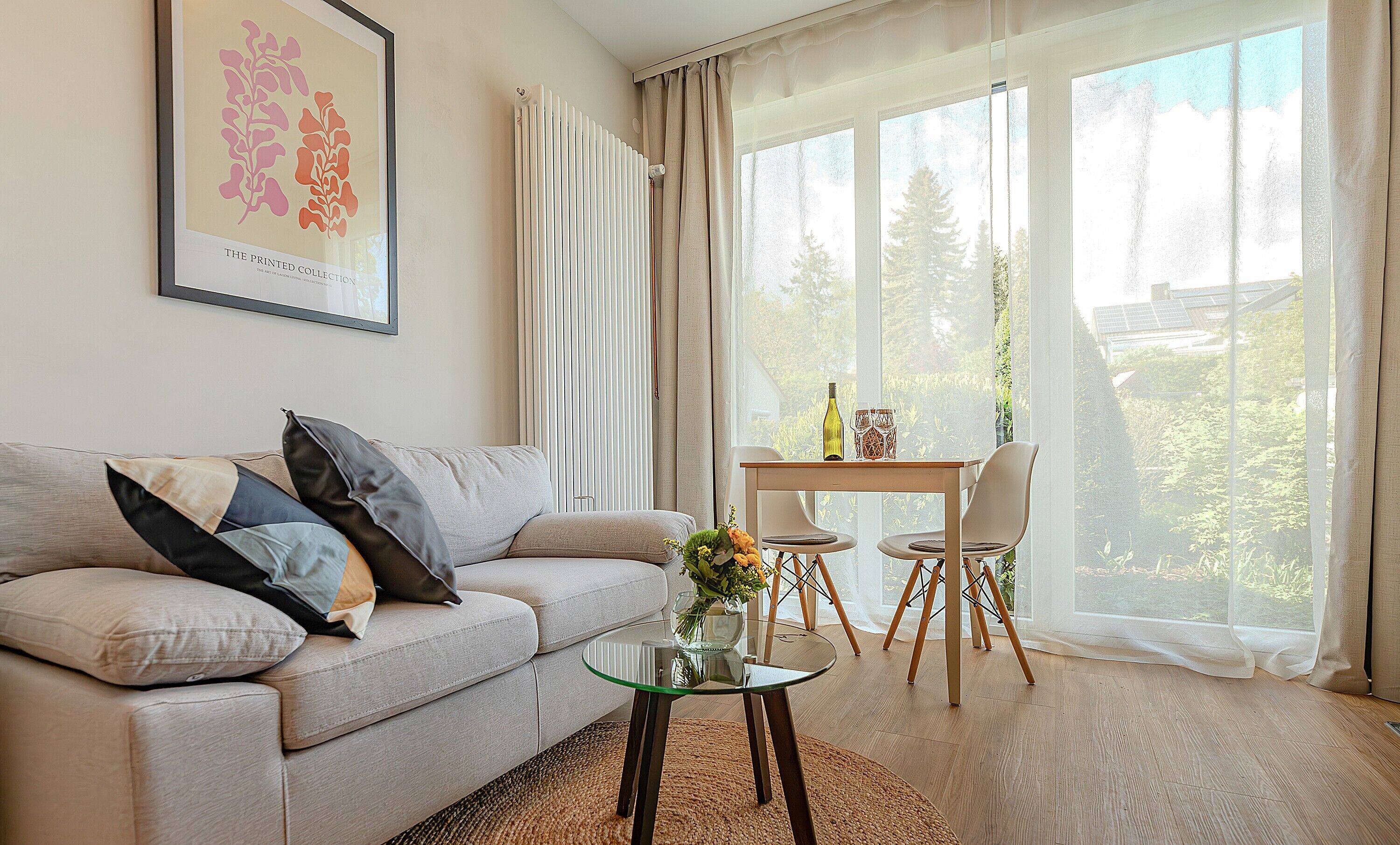 A living room with a sofa, a glass coffee table, a dining table with chairs, and a large window with curtains.