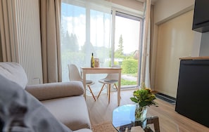 Una sala de estar moderna con un sofá, una mesa de centro de vidrio con un florero, una mesa de comedor con sillas y un puerta corrediza de vidrio que da a un balcón.