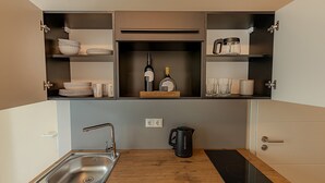 A compact kitchen with a built-in sink, a kettle, and wine bottles on the shelves. - Studio at the Vineyards (Iphofen)