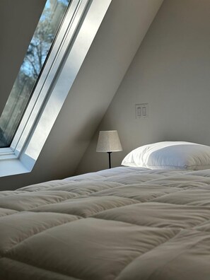 Une chambre avec un plafond en pente, une fenêtre, une lampe et un lit.