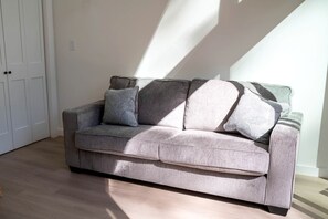 A grey sofa with patterned cushions in a room with wooden flooring and a white door.