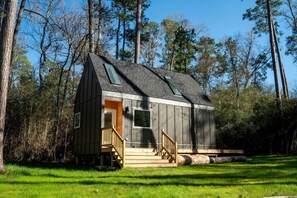 A small cabin with a sloped roof, a wooden staircase, and a door leading to an interior.