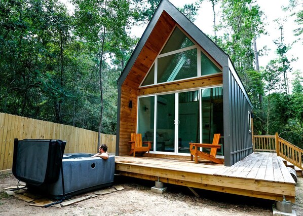 A cabin with a deck, a hot tub, and two chairs.
