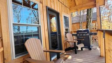 A wooden deck with two Adirondack chairs, a grill, and a covered porch with windows.