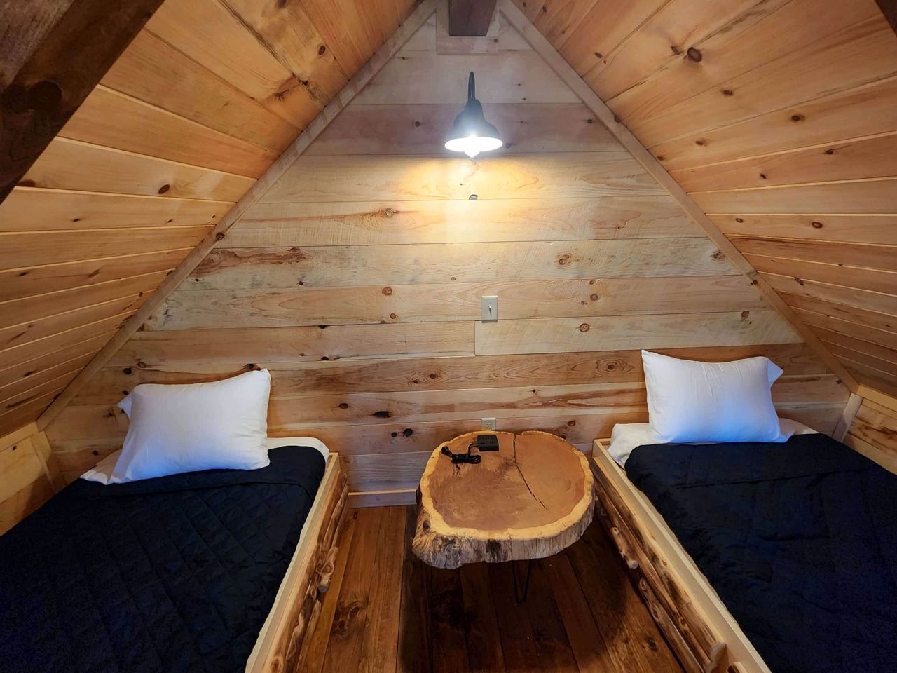 A cozy attic bedroom with two beds, a central wooden table, and a ceiling light.