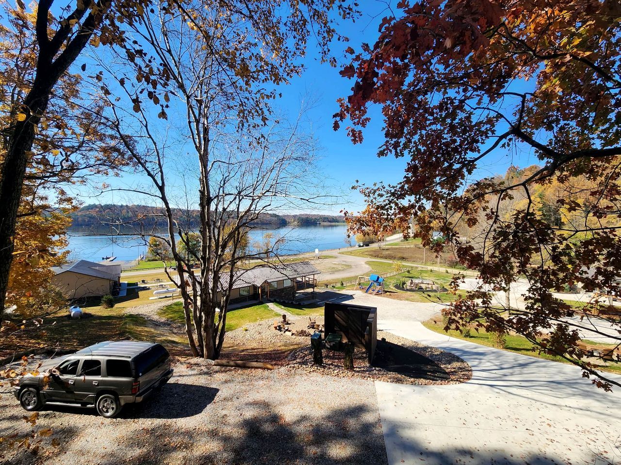 A campground with a vehicle parked near a tree, a picnic table, and a view of a lake.