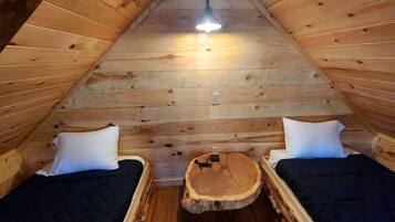 A cozy attic bedroom with two beds, a central wooden table, and a ceiling light.