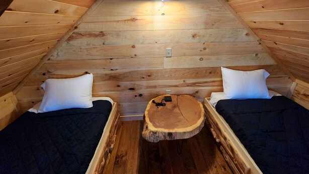 A cozy attic bedroom with two beds, a central wooden table, and a ceiling light. - Lofted Cabin Wonderful for Outdoor Adventures near Tappan Lake in Ohio (Deersville)