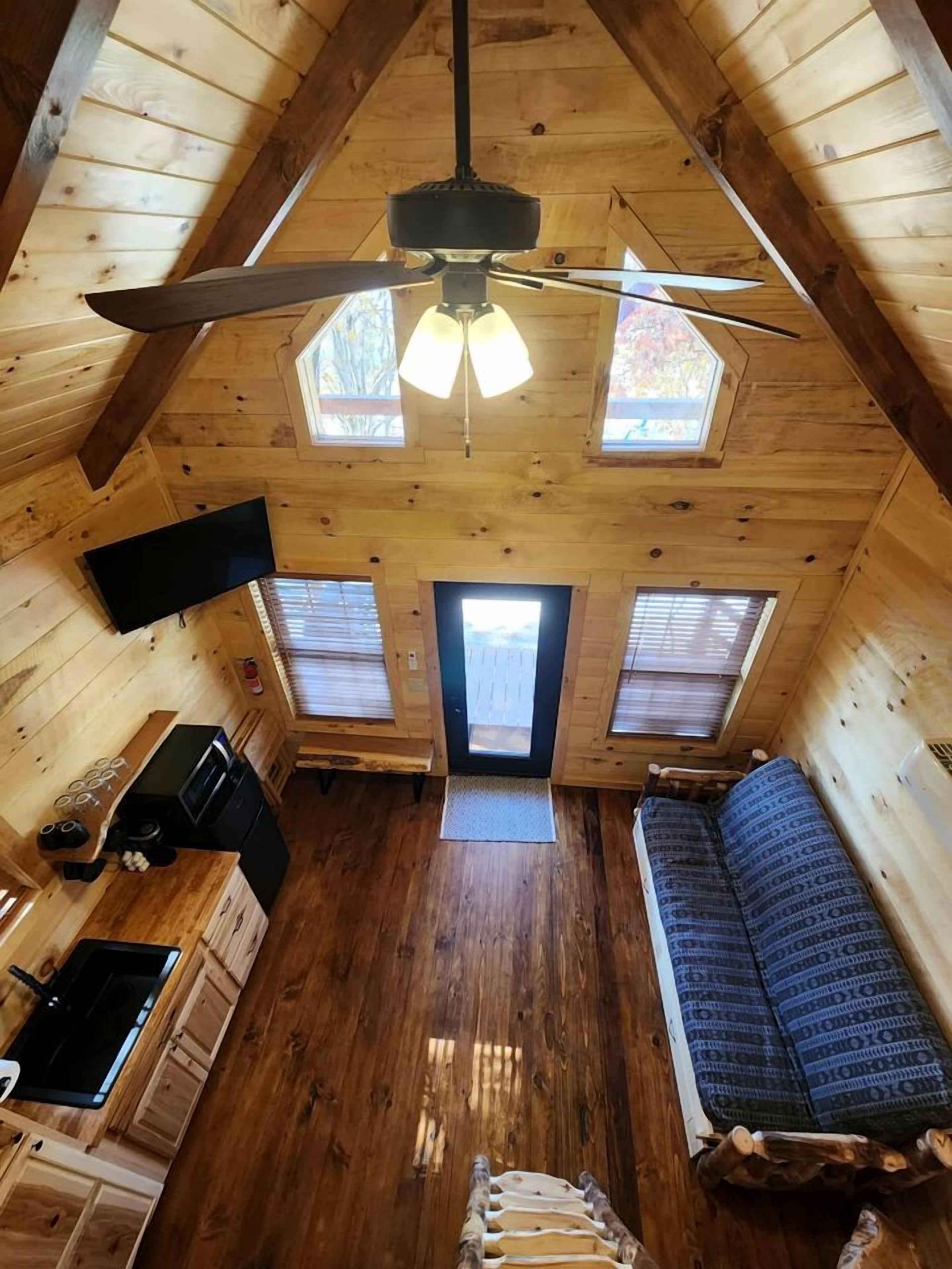 A cozy cabin with a loft bedroom, a kitchenette, and a large window.